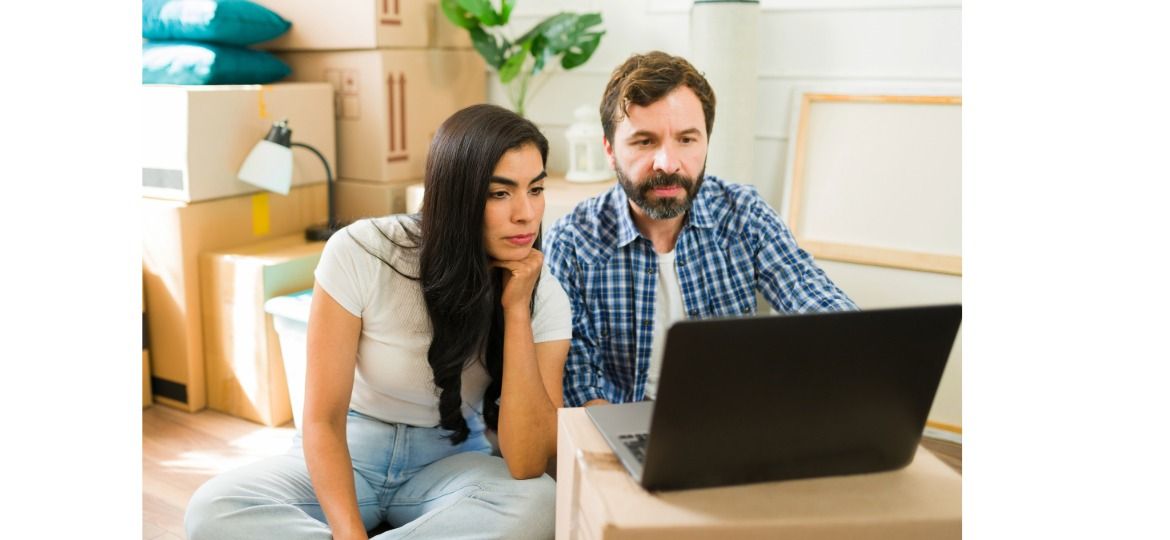 A worried couple sitting among moving boxes, looking at a laptop while reviewing their mortgage and foreclosure options