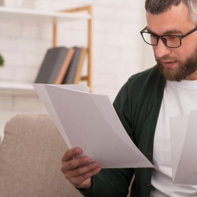 A New England homeowner holds the signed loan modification agreement the new mortgage company must honor, beside a servicing transfer notice.