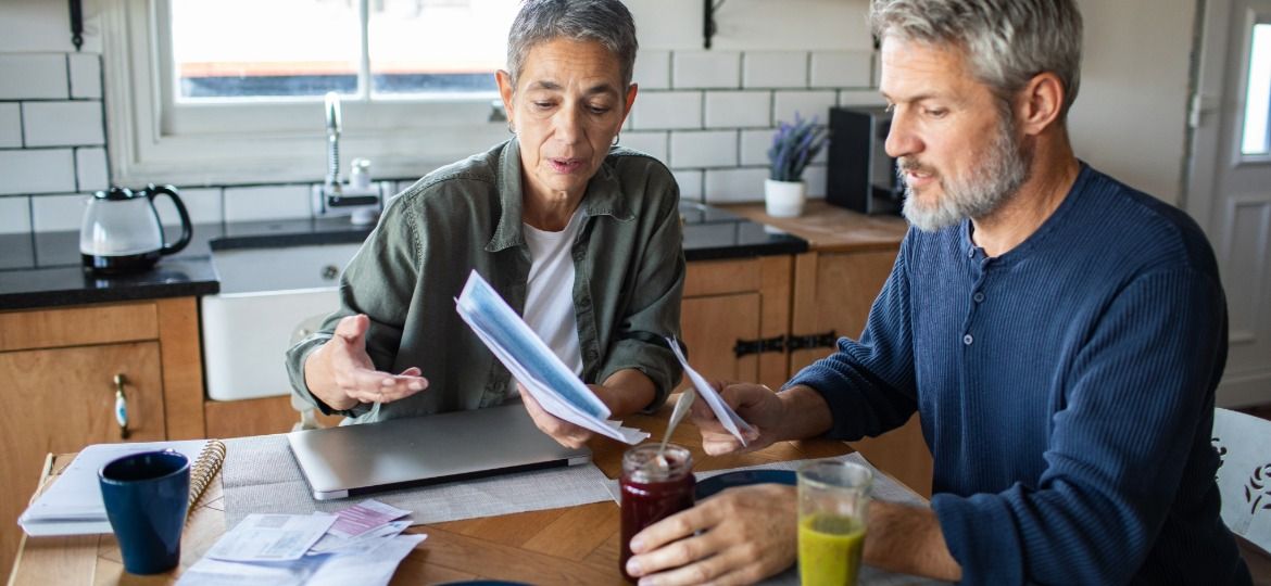 A couple sitting at their kitchen table going through household bills and paperwork together.